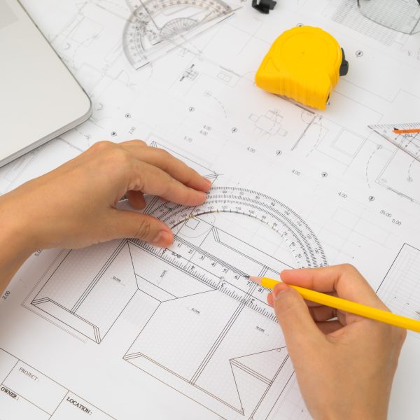 Hand over Construction plans with yellow helmet and drawing tools on blueprints